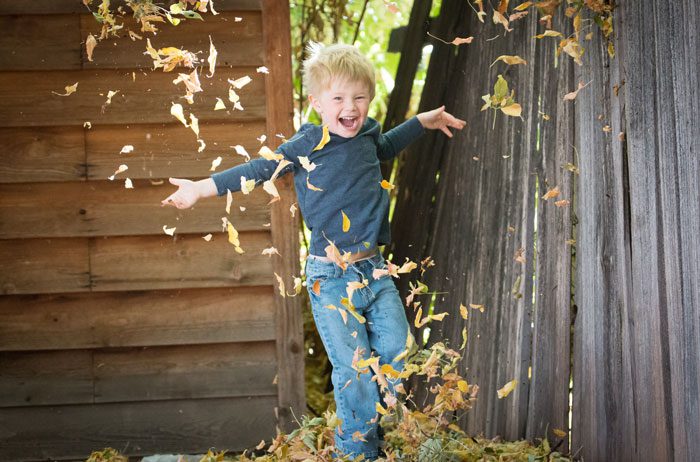 A happy boy playing in fall leaves.