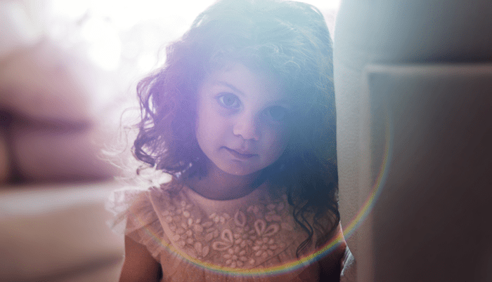 A girl with wavy hair and pink dress looking back at the camera.