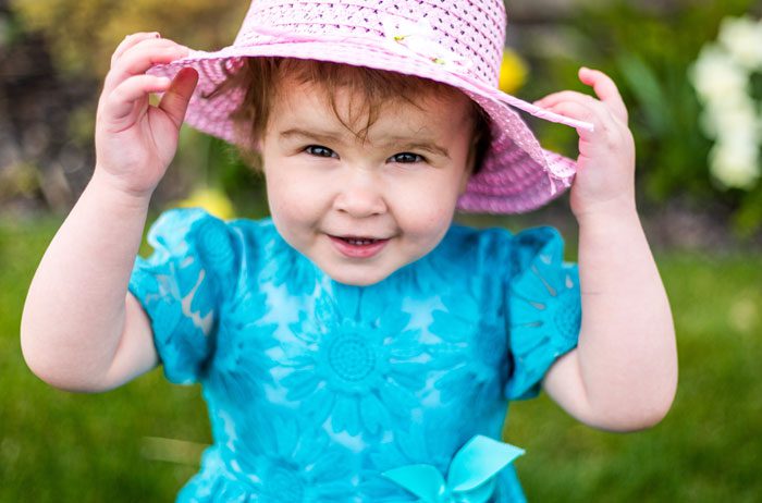 A girl in blue flower dress and pink hat.