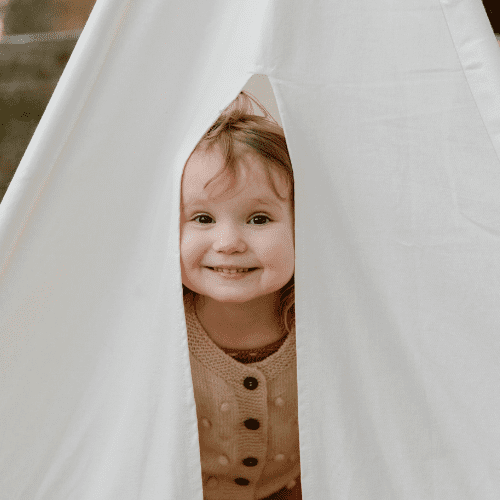 Happy little girl peeks outside of a tent